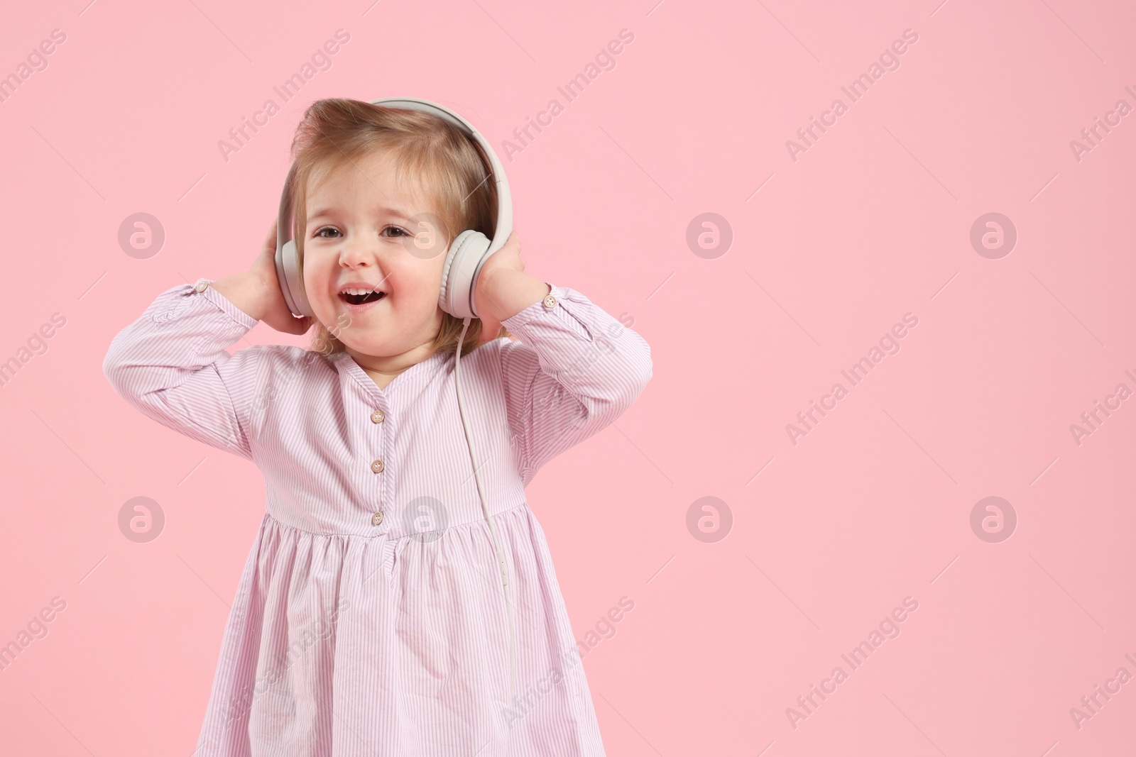 Cute little girl in headphones on pink background, space for text Photo of Cute little girl in headphones on pink background, space for text