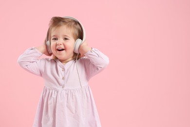 Photo of Cute little girl in headphones on pink background, space for text