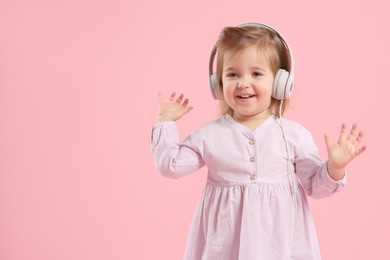 Photo of Cute little girl in headphones on pink background, space for text