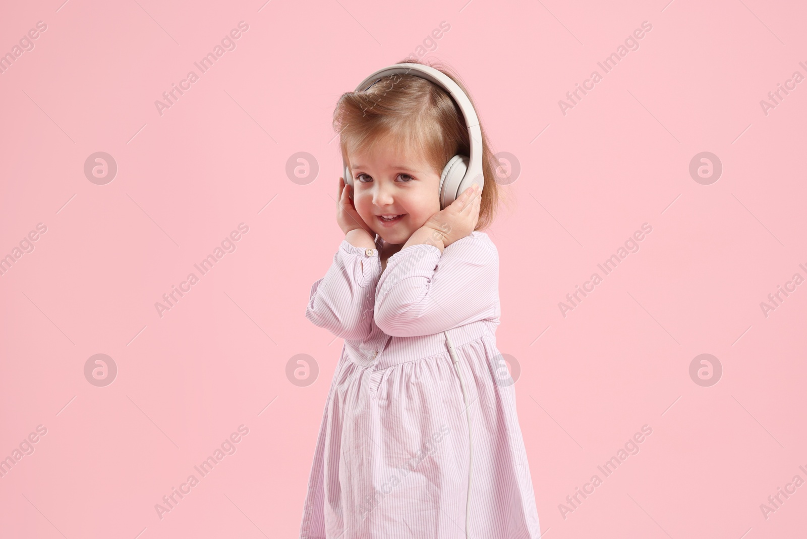 Photo of Cute little girl in headphones on pink background