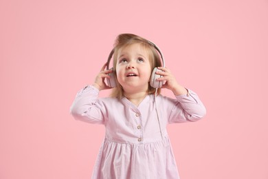 Photo of Cute little girl in headphones on pink background