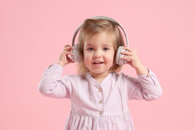Photo of Cute little girl in headphones on pink background