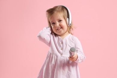 Photo of Cute little girl with headphones and microphone on pink background