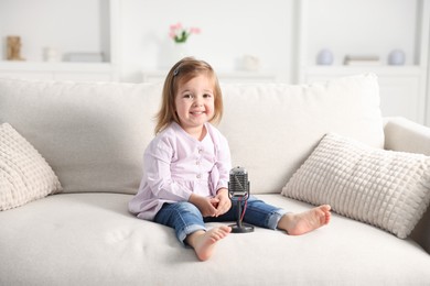 Photo of Cute little girl with microphone on sofa at home