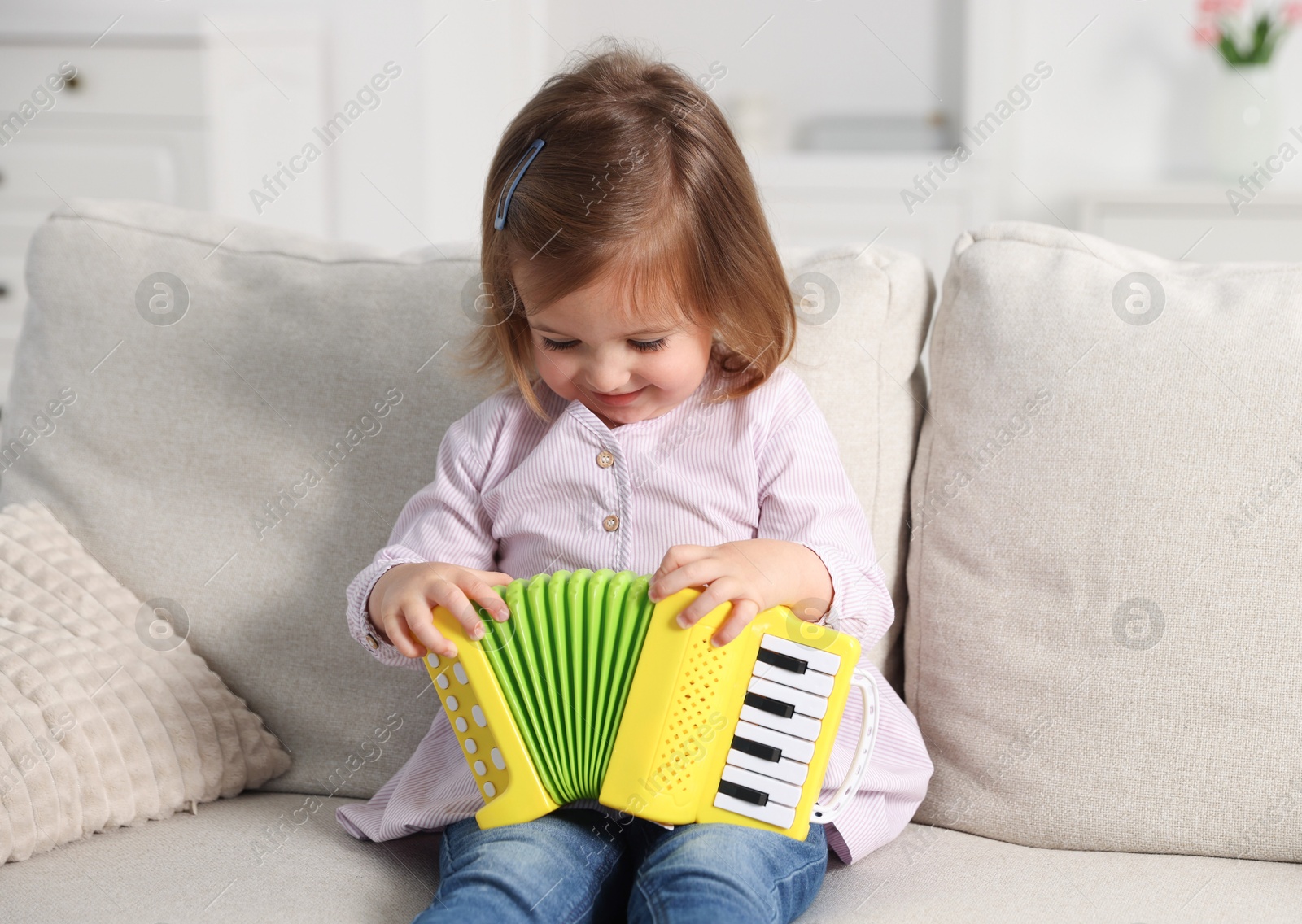 Cute little girl playing toy accordion on sofa at home Photo of Cute little girl playing toy accordion on sofa at home