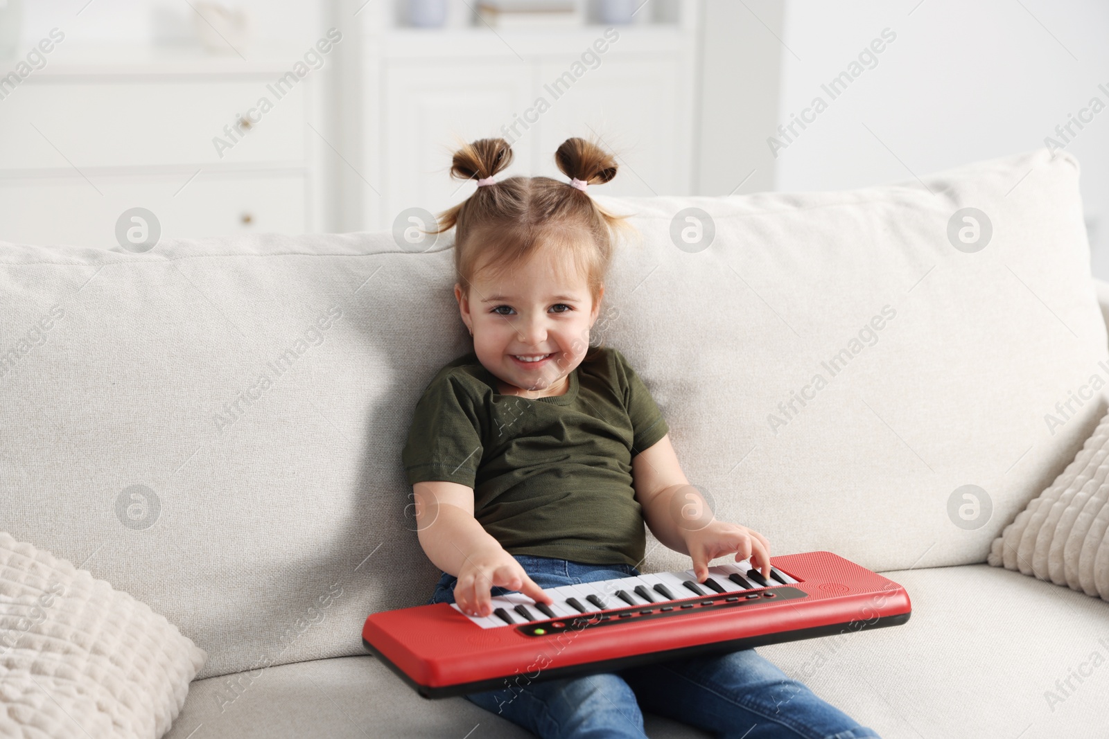 Cute little girl playing toy electric piano on sofa at home Photo of Cute little girl playing toy electric piano on sofa at home