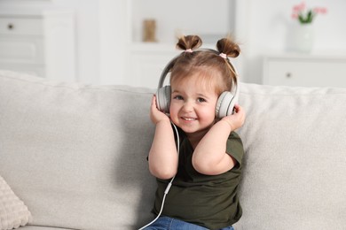 Photo of Cute little girl in headphones on sofa at home