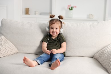 Photo of Cute little girl in headphones on sofa at home
