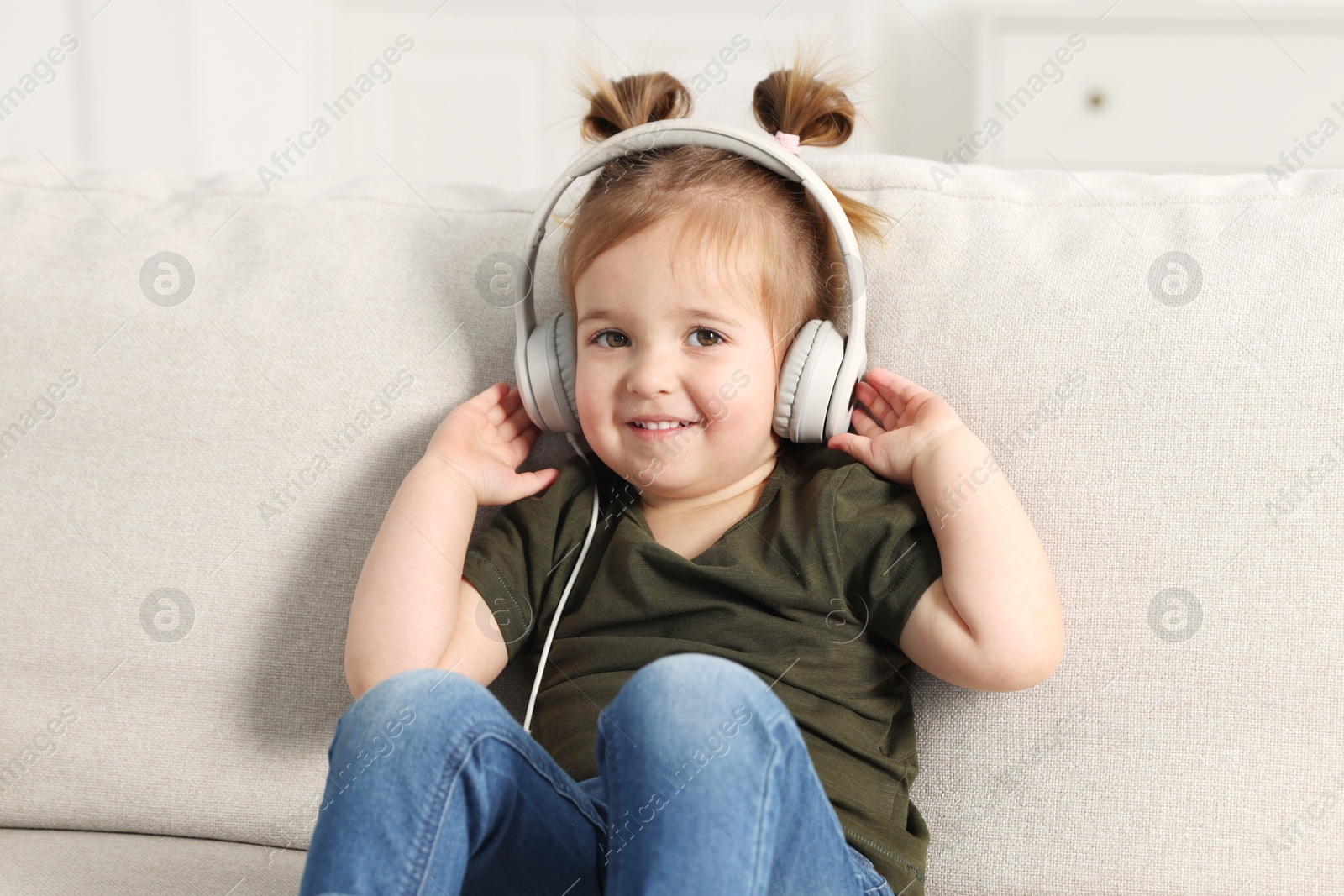 Cute little girl in headphones on sofa at home Photo of Cute little girl in headphones on sofa at home