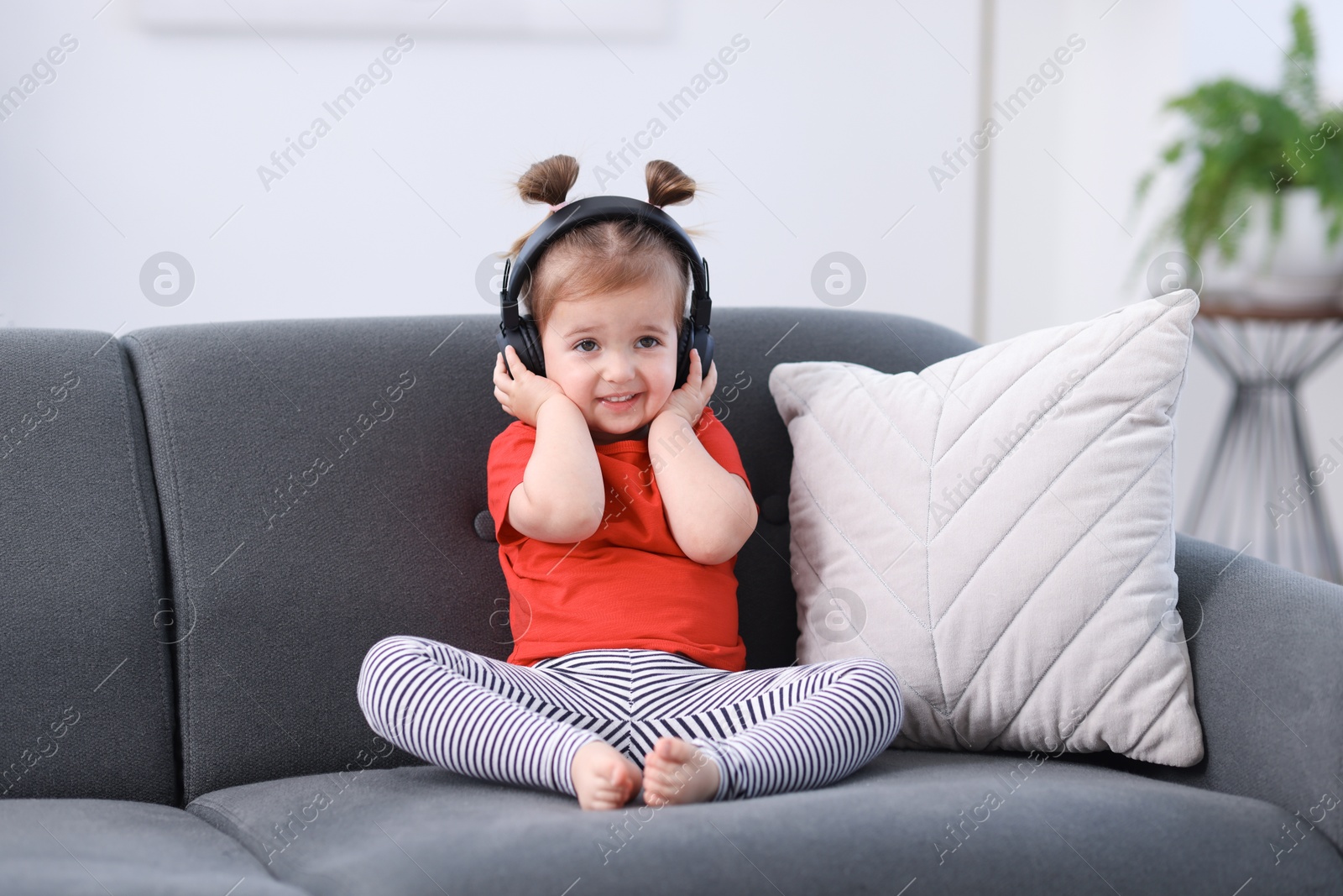 Cute little girl in headphones on sofa at home Photo of Cute little girl in headphones on sofa at home