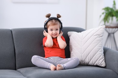 Photo of Cute little girl in headphones on sofa at home
