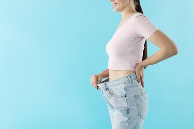 Photo of Woman wearing old jeans after weight loss on light blue background, closeup. Space for text