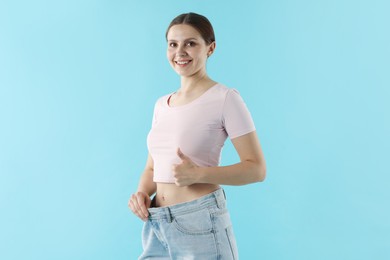 Photo of Beautiful woman wearing old jeans after weight loss and showing thumbs up on light blue background