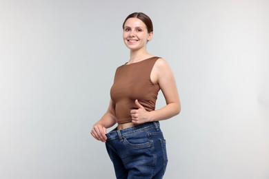 Photo of Beautiful woman wearing old jeans after weight loss and showing thumbs up on light grey background