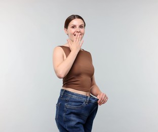 Photo of Beautiful woman wearing old jeans after weight loss on light grey background