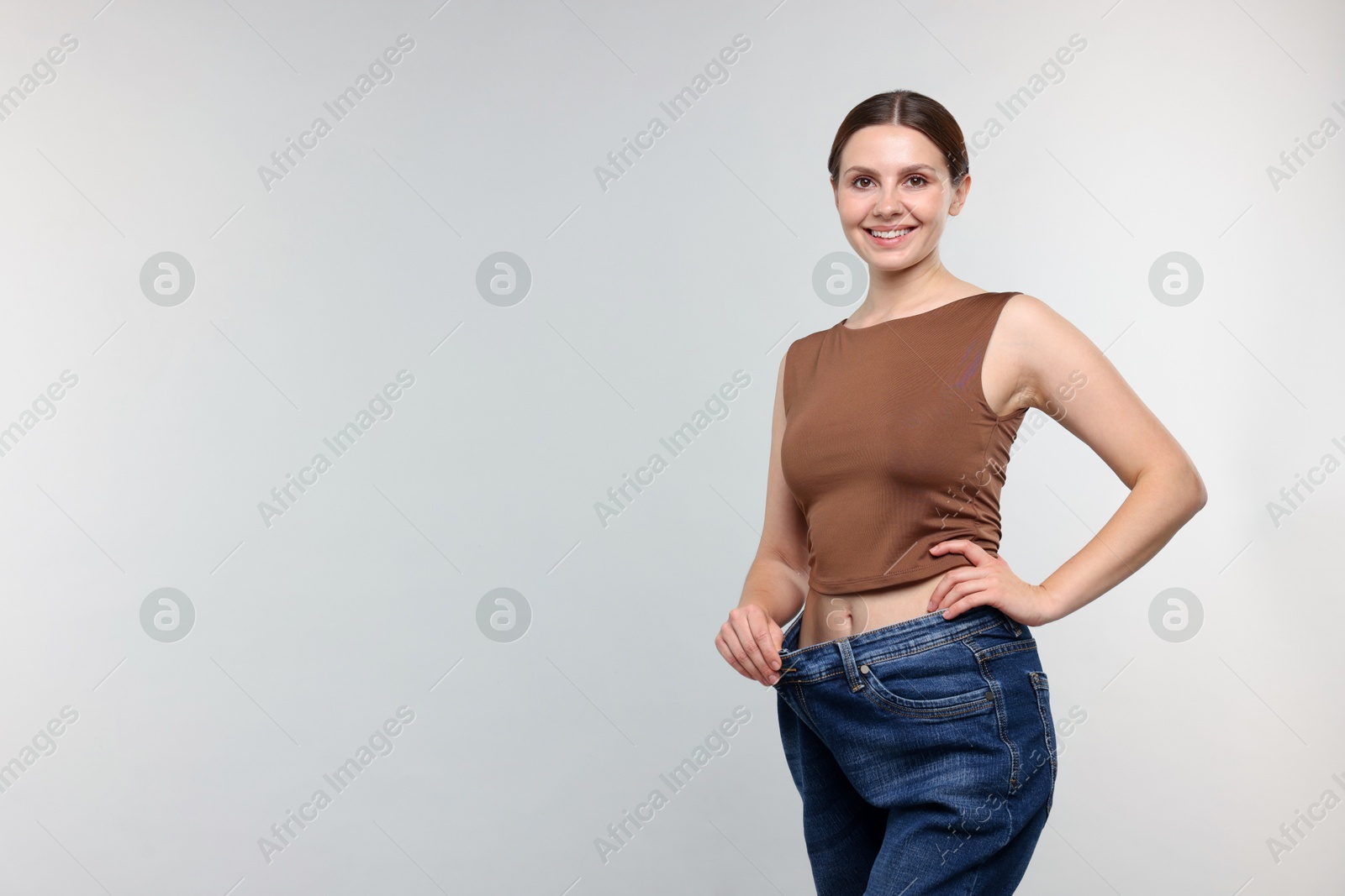 Beautiful woman wearing old jeans after weight loss on light grey background, space for text Photo of Beautiful woman wearing old jeans after weight loss on light grey background, space for text