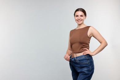 Photo of Beautiful woman wearing old jeans after weight loss on light grey background, space for text