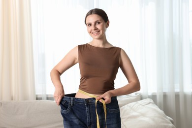 Photo of Beautiful woman with measuring tape wearing old jeans after weight loss indoors