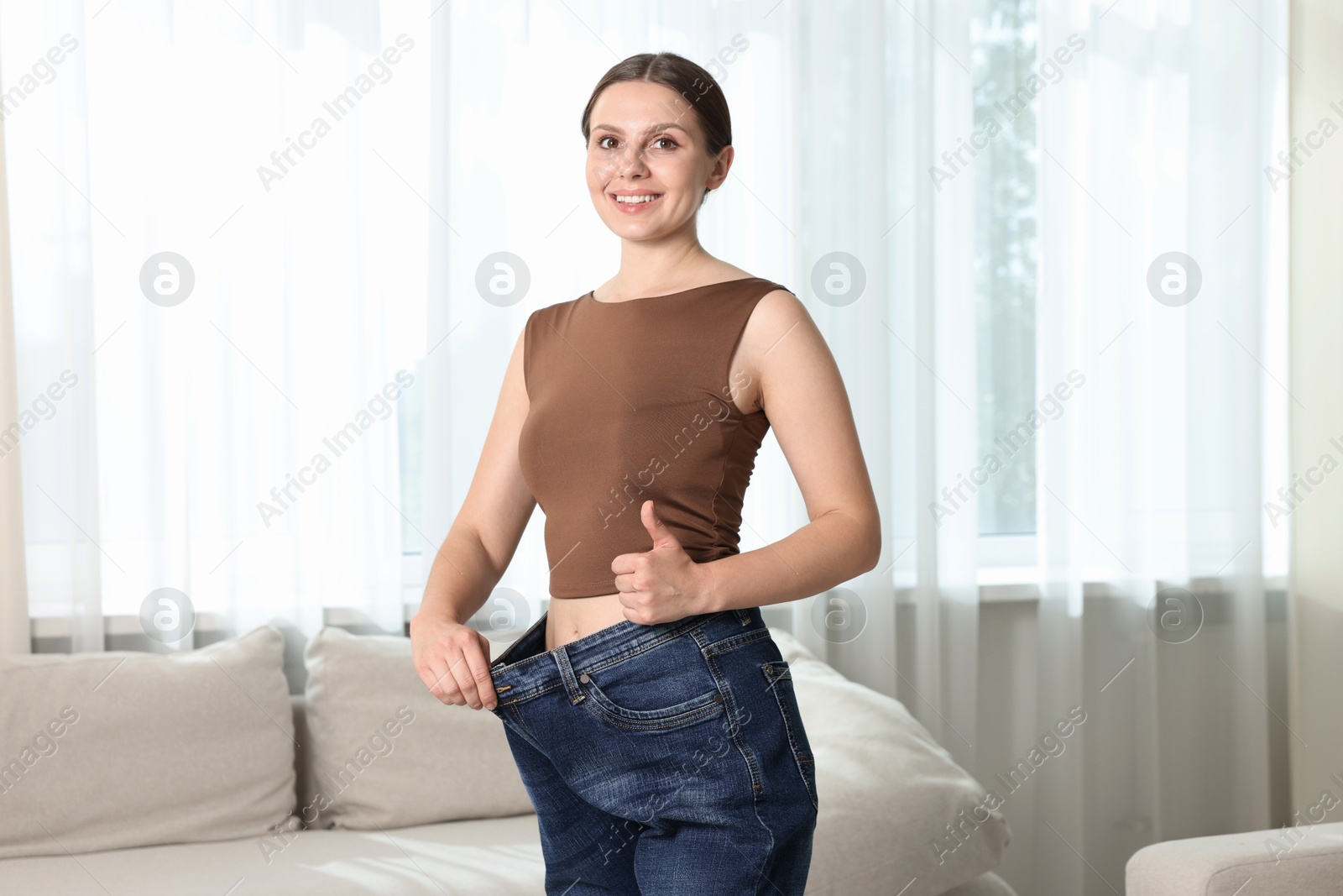 Beautiful woman wearing old jeans after weight loss and showing thumbs up indoors Photo of Beautiful woman wearing old jeans after weight loss and showing thumbs up indoors
