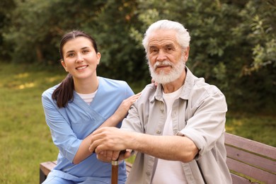 Photo of Portrait of smiling nurse and elderly man with walking cane outdoors