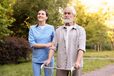 Photo of Smiling nurse supporting elderly man who using walking frame outdoors