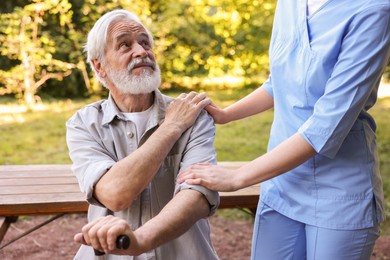 Photo of Nurse supporting elderly man with walking cane outdoors, closeup