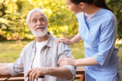 Photo of Nurse supporting elderly man with walking cane outdoors, closeup