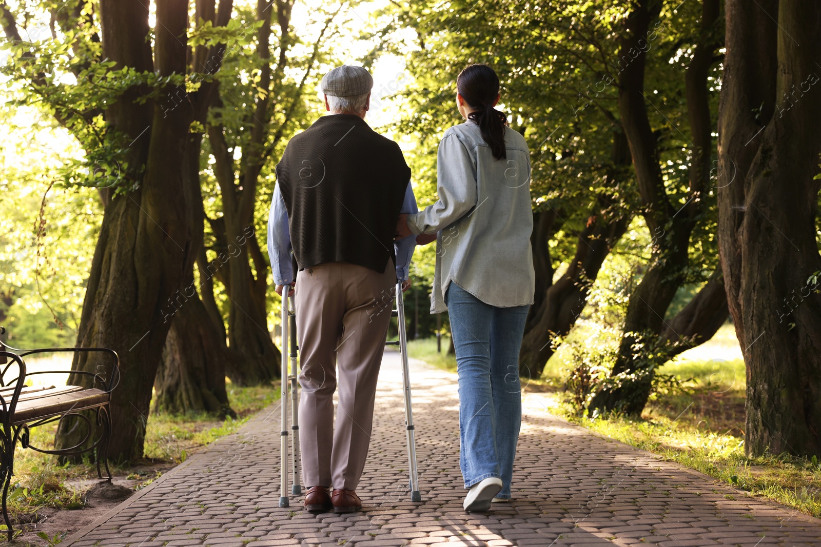 Caregiver supporting elderly man who using walking frame outdoors, back view Photo of Caregiver supporting elderly man who using walking frame outdoors, back view