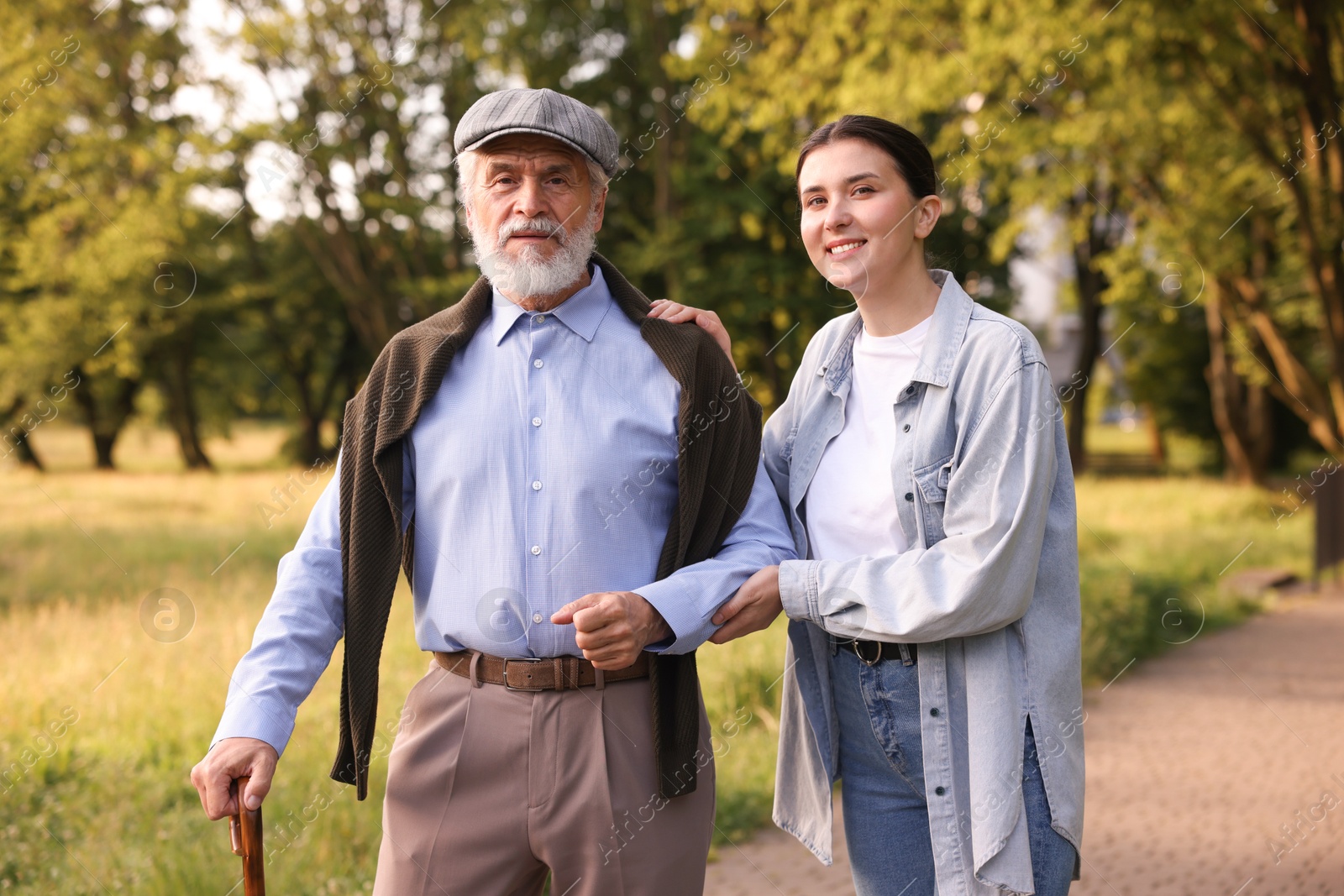 Smiling caregiver supporting elderly man with walking cane outdoors Photo of Smiling caregiver supporting elderly man with walking cane outdoors