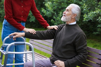 Photo of Caregiver supporting elderly man with walking frame outdoors, closeup