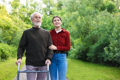 Photo of Smiling caregiver supporting elderly man who using walking frame outdoors. Space for text