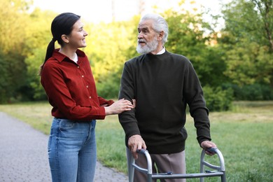 Photo of Smiling caregiver supporting elderly man who using walking frame outdoors