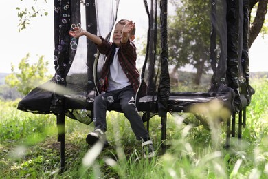 Photo of Happy boy playing with soap bubbles on trampoline outdoors