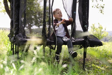 Photo of Happy boy playing with soap bubbles on trampoline outdoors