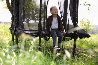 Photo of Happy boy sitting on black trampoline outdoors