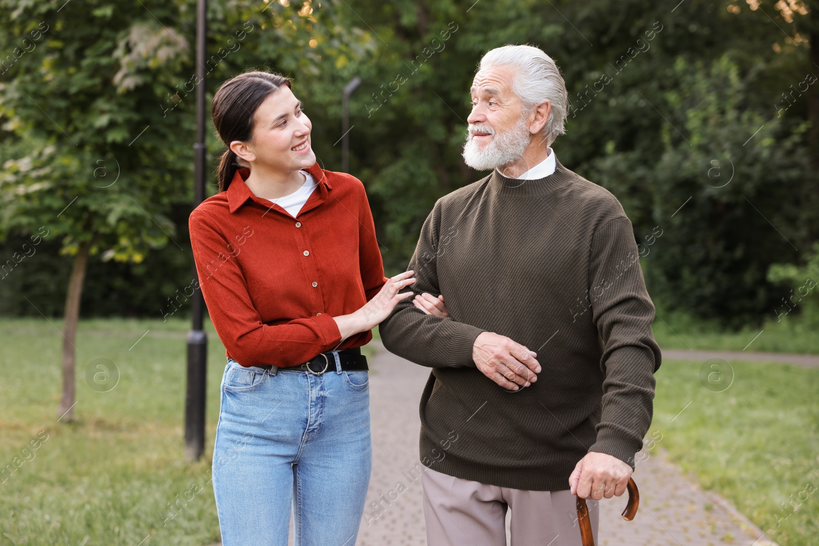 Smiling caregiver supporting elderly man who using walking cane outdoors Photo of Smiling caregiver supporting elderly man who using walking cane outdoors