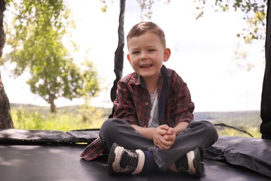 Photo of Happy boy sitting on black trampoline outdoors