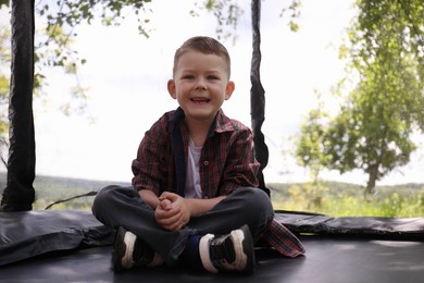 Photo of Happy boy sitting on black trampoline outdoors