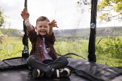 Photo of Happy boy playing with soap bubbles on trampoline outdoors
