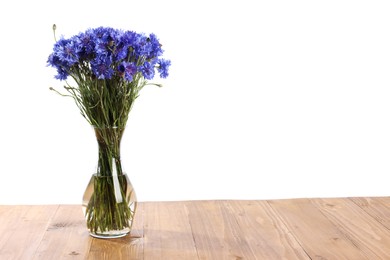 Photo of Beautiful blue cornflowers in vase on wooden table against white background