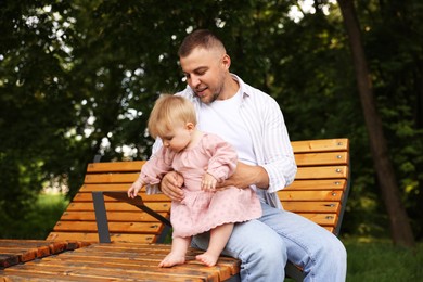 Photo of Smiling dad and his newborn girl on bench outdoors. Happy Father's Day