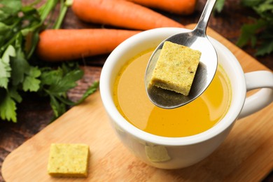 Photo of Putting aromatic bouillon cube into broth at wooden table, above view