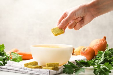 Photo of Woman putting aromatic bouillon cube into broth at table, closeup