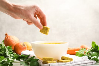 Photo of Woman putting aromatic bouillon cube into broth at table, closeup