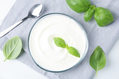 Photo of Tasty yoghurt with basil in bowl on white table, flat lay