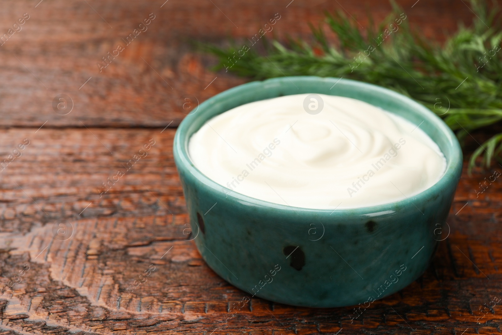 Photo of Tasty sour cream with dill on wooden table, closeup. Space for text