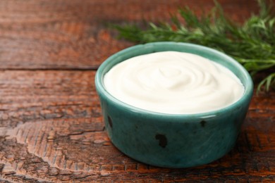 Photo of Tasty sour cream with dill on wooden table, closeup. Space for text