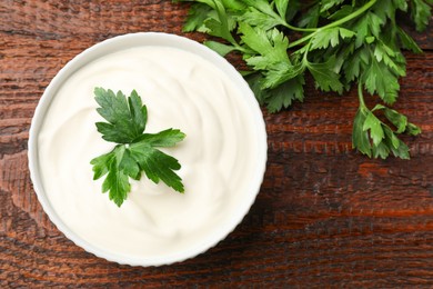 Photo of Tasty sour cream with parsley on wooden table, flat lay
