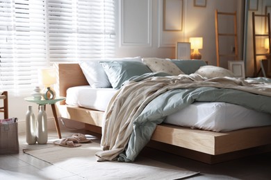 Photo of Comfortable bed with soft linens, lamp and decor in stylish room. Home textile