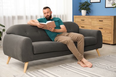 Photo of Harmony. Man reading book on sofa at home